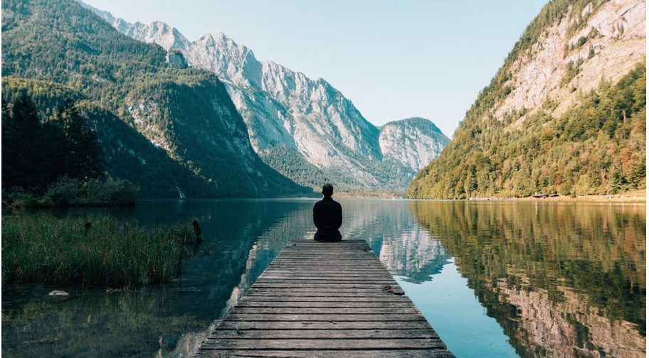 person sitting on the end of a dock on a lake