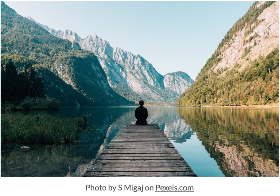 person sitting on the end of a dock on a lake